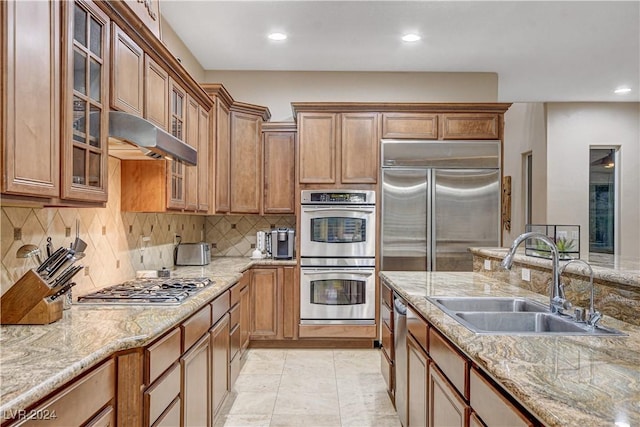 kitchen with decorative backsplash, appliances with stainless steel finishes, light stone counters, and sink