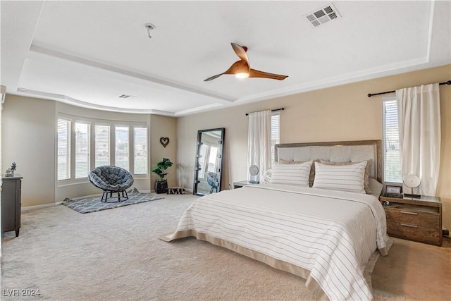 carpeted bedroom with a raised ceiling and ceiling fan