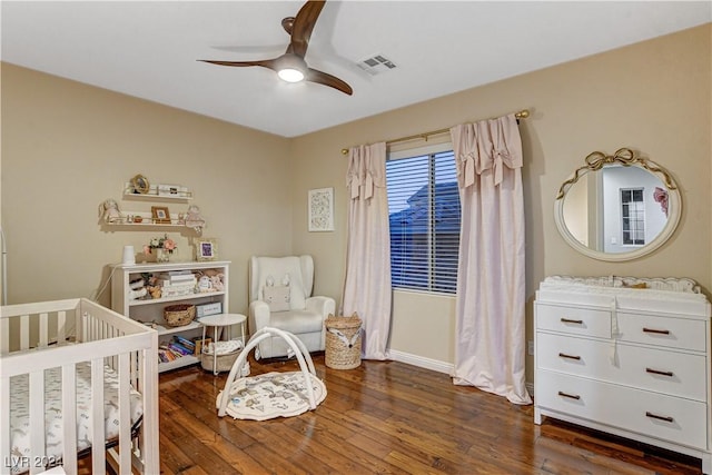 bedroom with ceiling fan, dark hardwood / wood-style floors, and a crib