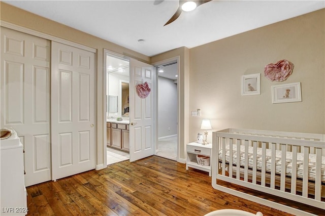 bedroom featuring ensuite bathroom, ceiling fan, dark wood-type flooring, a crib, and a closet