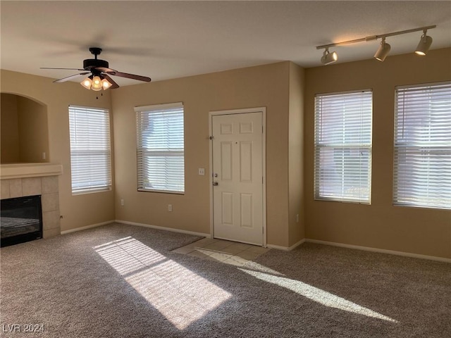 unfurnished living room with ceiling fan, light colored carpet, rail lighting, and a tiled fireplace