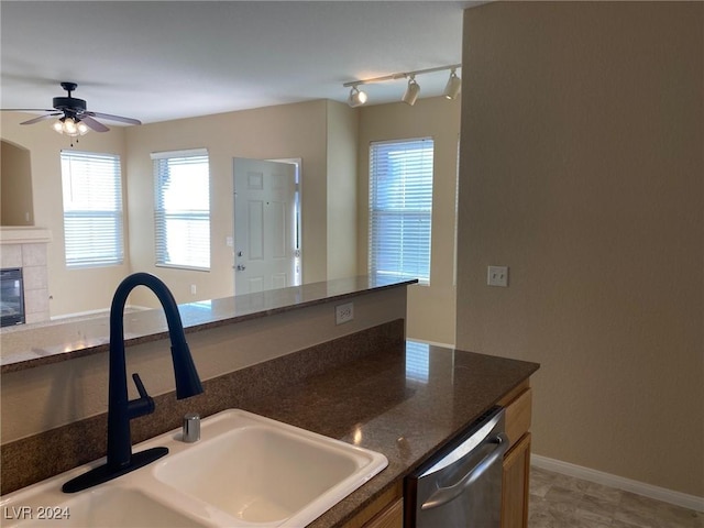 kitchen featuring stainless steel dishwasher, ceiling fan, sink, a tile fireplace, and light tile patterned floors