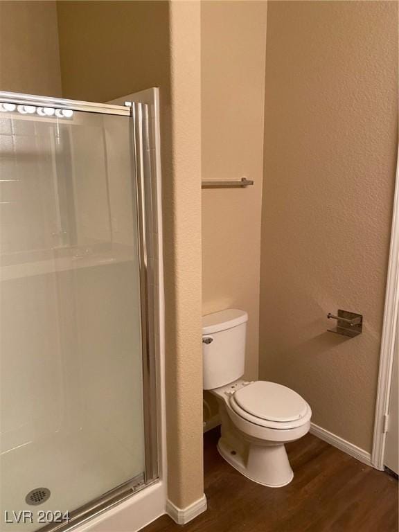 bathroom featuring wood-type flooring, toilet, and a shower with shower door