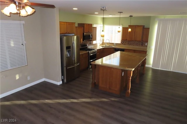 kitchen with sink, hanging light fixtures, appliances with stainless steel finishes, dark hardwood / wood-style floors, and a kitchen island