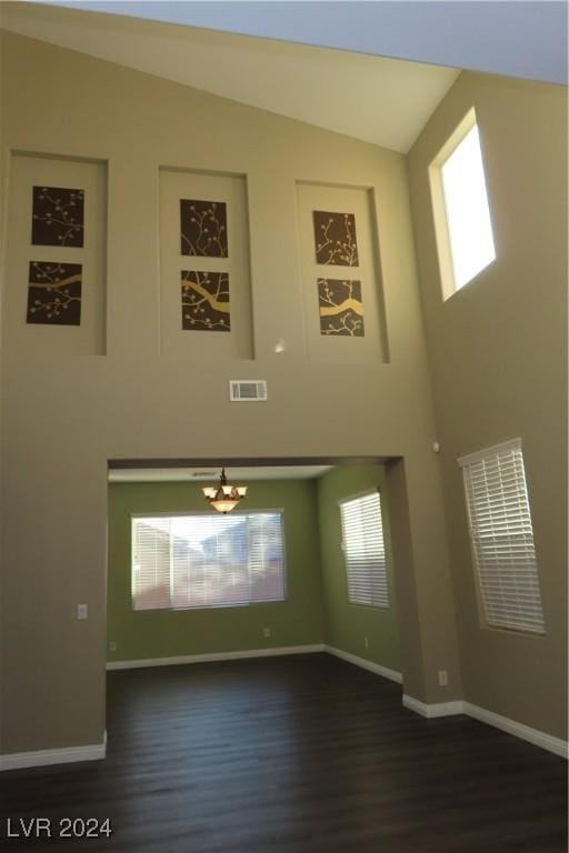 unfurnished living room featuring high vaulted ceiling, an inviting chandelier, and dark hardwood / wood-style flooring