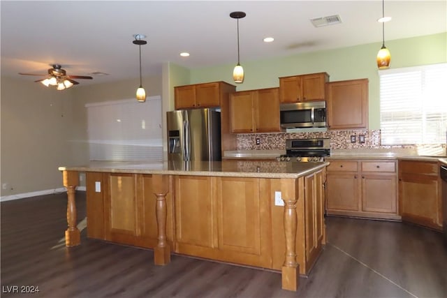 kitchen featuring dark wood-type flooring, decorative light fixtures, a center island, appliances with stainless steel finishes, and backsplash