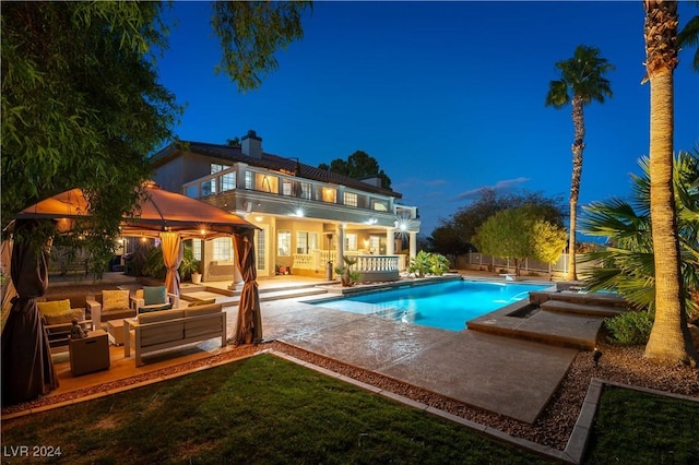 pool at night featuring outdoor lounge area, a jacuzzi, and a patio