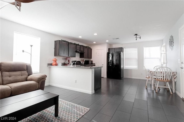 kitchen with kitchen peninsula, black fridge, dark brown cabinets, and sink