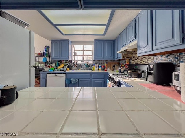 kitchen with backsplash, white dishwasher, blue cabinetry, tile counters, and stainless steel range oven