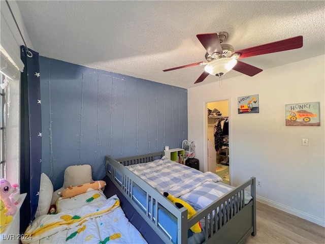 bedroom with ceiling fan, a textured ceiling, a walk in closet, a closet, and light wood-type flooring