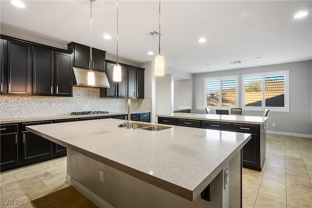 kitchen featuring sink, stainless steel gas cooktop, decorative light fixtures, decorative backsplash, and a center island with sink