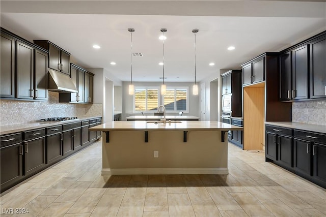 kitchen featuring sink, stainless steel gas cooktop, a kitchen breakfast bar, decorative light fixtures, and a kitchen island with sink