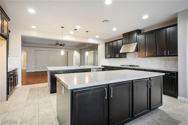 kitchen featuring ceiling fan, sink, stainless steel appliances, decorative light fixtures, and a center island with sink