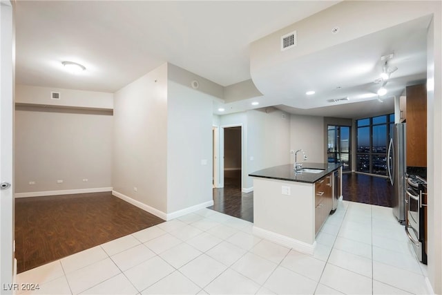 kitchen with stainless steel appliances, sink, light hardwood / wood-style floors, and a center island with sink