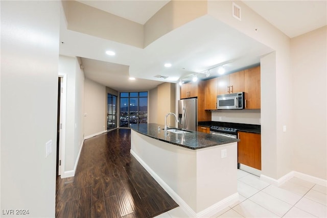 kitchen featuring dark stone counters, stainless steel appliances, a kitchen island with sink, sink, and light hardwood / wood-style floors