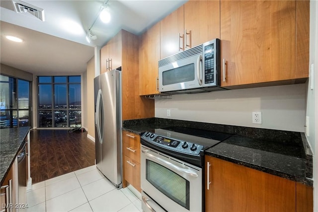 200 W Sahara Ave Unit 1510, Las Vegas, NV 89102 - kitchen with stainless steel appliances, dark stone counters, brown cabinetry, light tile patterned floors, and rail lighting