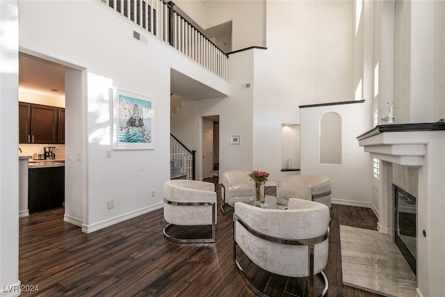 living room with a towering ceiling, dark hardwood / wood-style floors, and a premium fireplace