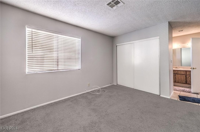 unfurnished bedroom featuring light colored carpet, a textured ceiling, and a closet