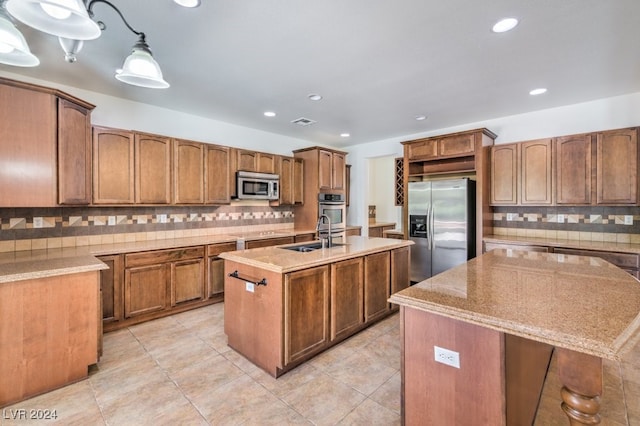 kitchen featuring tasteful backsplash, a kitchen island with sink, stainless steel appliances, and decorative light fixtures