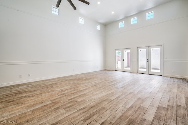 empty room featuring ceiling fan, light wood-type flooring, a towering ceiling, and french doors