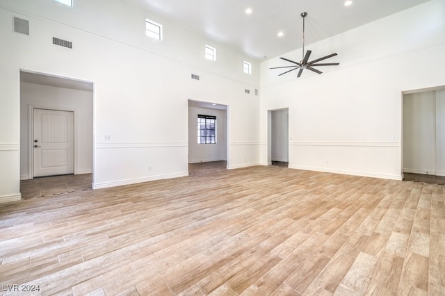 unfurnished living room with ceiling fan, light hardwood / wood-style floors, and a towering ceiling