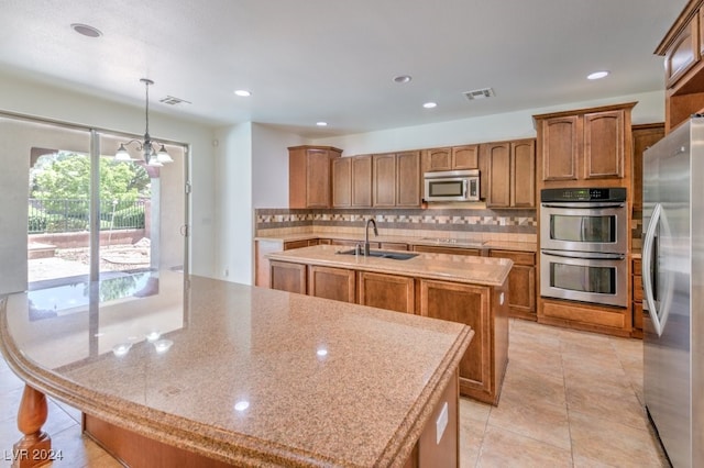 kitchen with a center island with sink, sink, hanging light fixtures, and appliances with stainless steel finishes