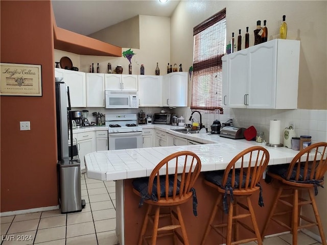 kitchen featuring kitchen peninsula, a breakfast bar, white appliances, sink, and white cabinetry