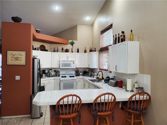 kitchen featuring white cabinetry, kitchen peninsula, tile countertops, white appliances, and a breakfast bar area