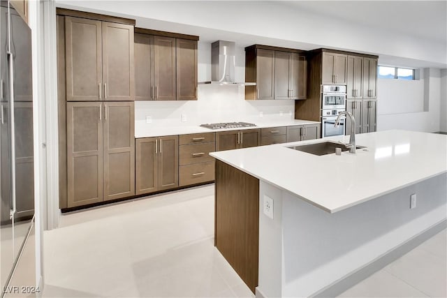 kitchen featuring sink, dark brown cabinetry, a kitchen island with sink, appliances with stainless steel finishes, and wall chimney exhaust hood