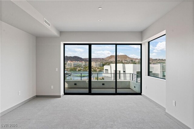 empty room with light carpet, a water view, baseboards, and visible vents