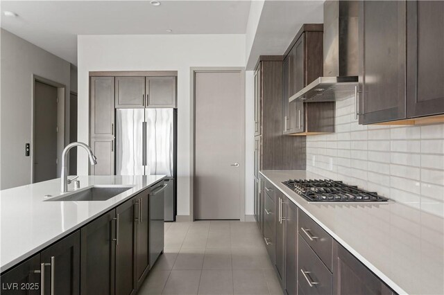 kitchen featuring wall chimney exhaust hood, appliances with stainless steel finishes, a sink, light countertops, and backsplash