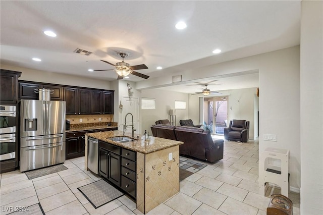 kitchen with sink, ceiling fan, an island with sink, dark brown cabinets, and stainless steel appliances