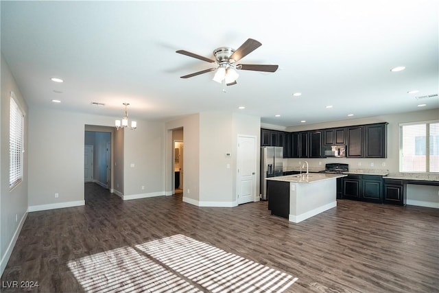 kitchen with appliances with stainless steel finishes, ceiling fan with notable chandelier, dark wood-type flooring, pendant lighting, and a center island with sink