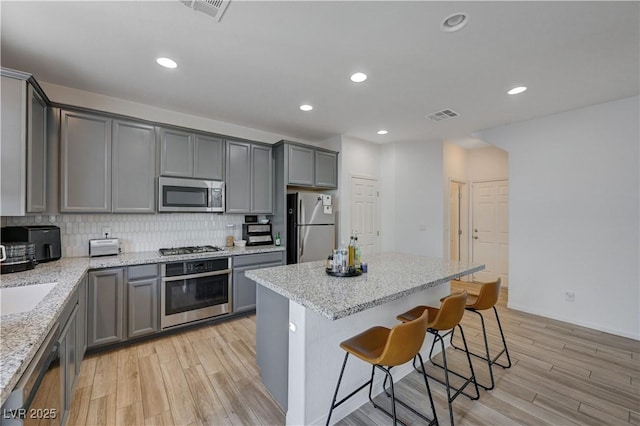 kitchen with light stone counters, appliances with stainless steel finishes, gray cabinetry, and tasteful backsplash