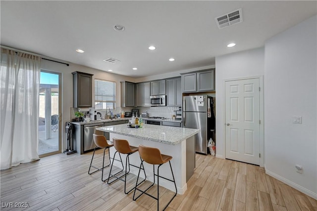 kitchen featuring appliances with stainless steel finishes, backsplash, a kitchen island, light stone counters, and a breakfast bar