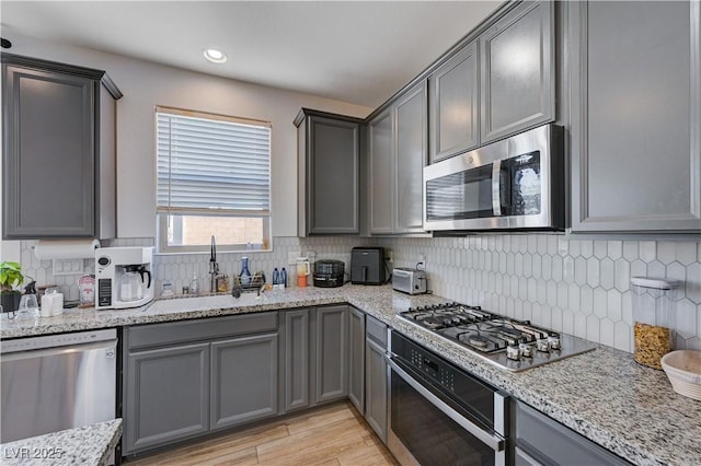 kitchen featuring gray cabinets, stainless steel appliances, light wood-type flooring, light stone countertops, and sink