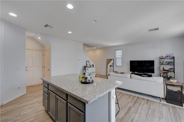 kitchen featuring light hardwood / wood-style flooring, light stone countertops, a kitchen breakfast bar, and a center island