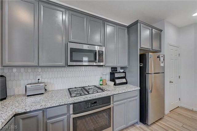 kitchen featuring gray cabinetry, light wood-type flooring, appliances with stainless steel finishes, and light stone counters