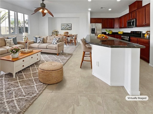 kitchen with ceiling fan, a center island, a breakfast bar, light tile patterned floors, and appliances with stainless steel finishes