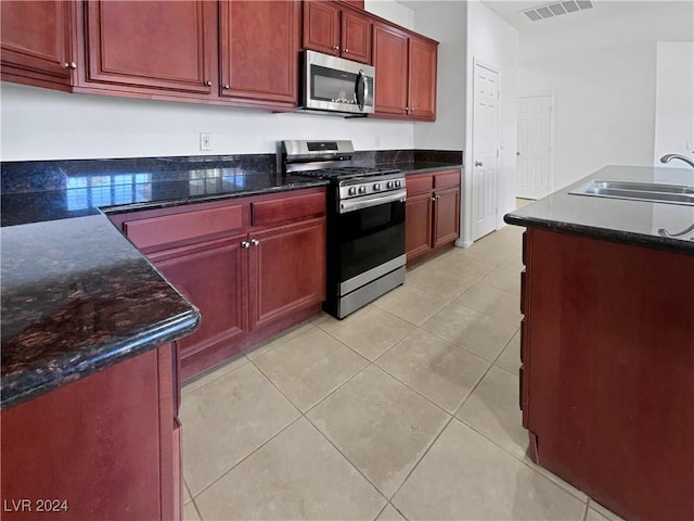 kitchen with dark stone countertops, light tile patterned floors, sink, and appliances with stainless steel finishes