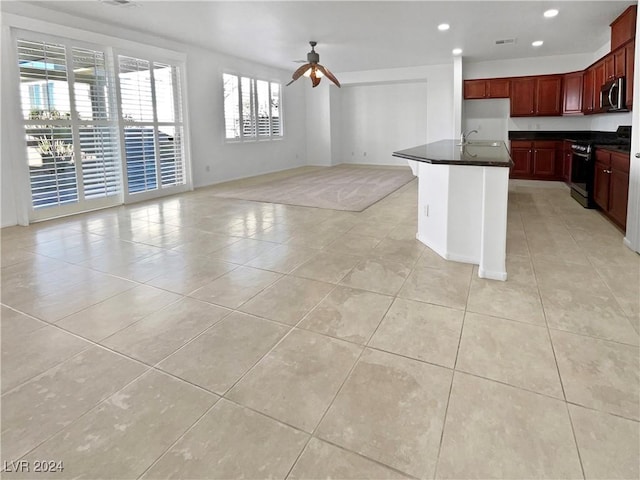 kitchen with ceiling fan, light tile patterned flooring, stove, and an island with sink