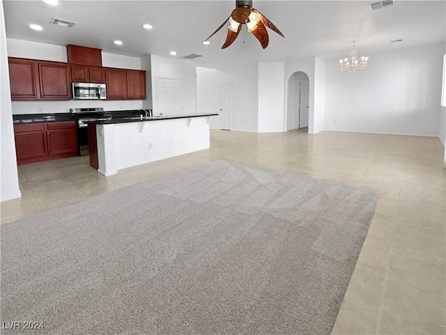 kitchen with appliances with stainless steel finishes, a breakfast bar, light tile patterned flooring, ceiling fan with notable chandelier, and a center island with sink