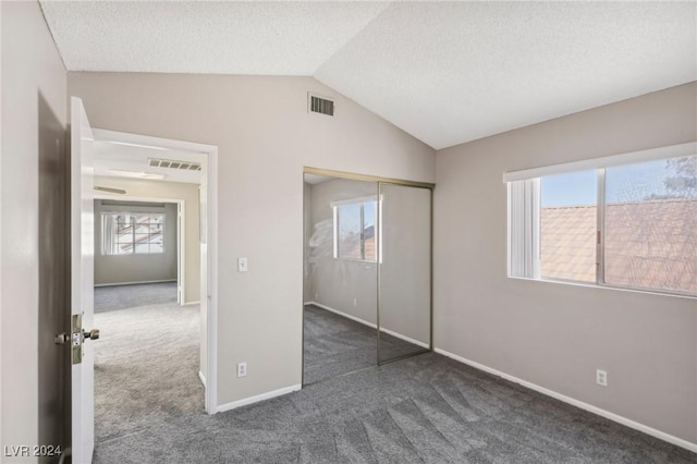 unfurnished bedroom with vaulted ceiling, multiple windows, dark carpet, and a closet