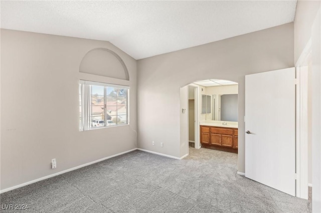 unfurnished bedroom featuring connected bathroom, light colored carpet, and vaulted ceiling