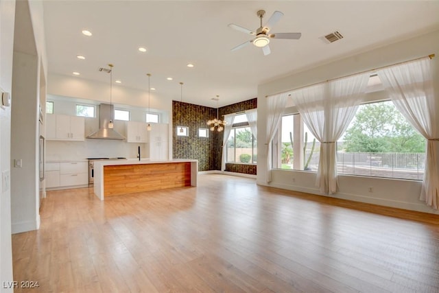 kitchen featuring pendant lighting, a center island, white cabinets, wall chimney range hood, and plenty of natural light