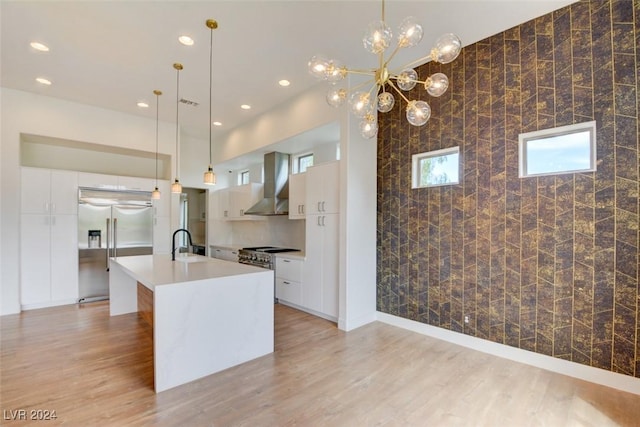 kitchen featuring a kitchen island with sink, decorative light fixtures, wall chimney range hood, and appliances with stainless steel finishes