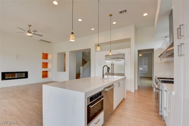 kitchen with pendant lighting, premium appliances, white cabinets, and a kitchen island with sink