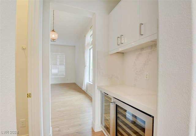 bar with white cabinets, decorative light fixtures, light hardwood / wood-style floors, and wine cooler