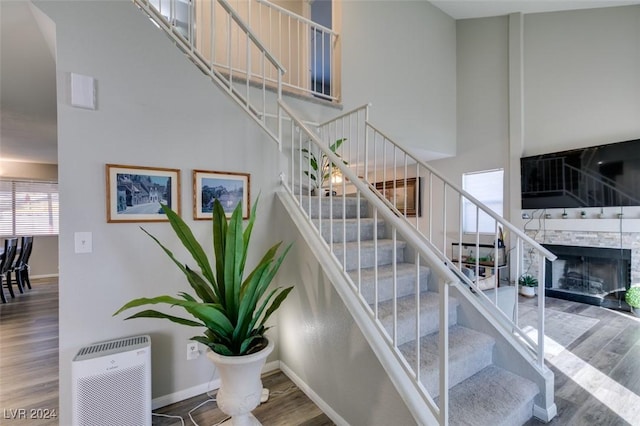 stairway with a fireplace, wood-type flooring, and a towering ceiling