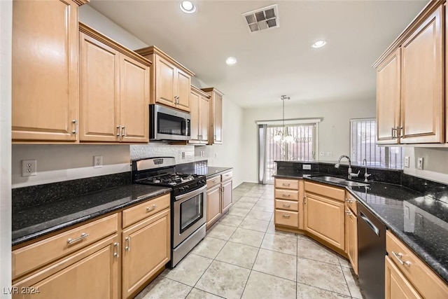 kitchen with appliances with stainless steel finishes, dark stone counters, sink, decorative light fixtures, and a notable chandelier